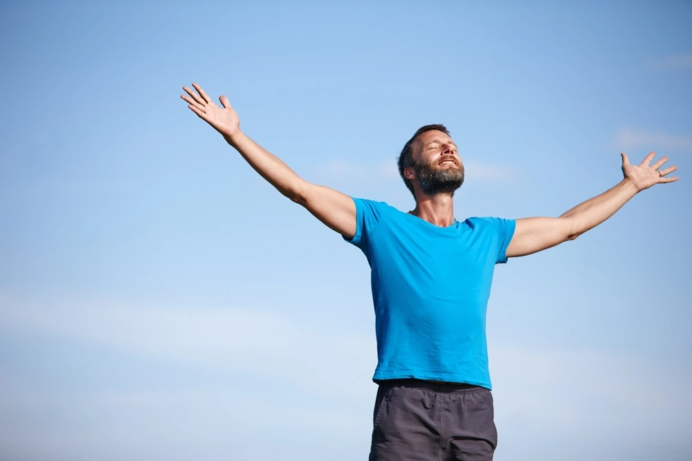 A happy man with arms open while breathing in fresh air