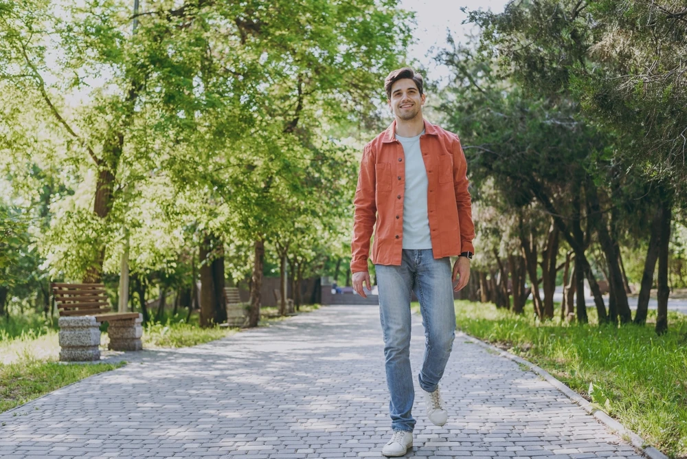 A man is taking a walk at the park as part of his self-care routine