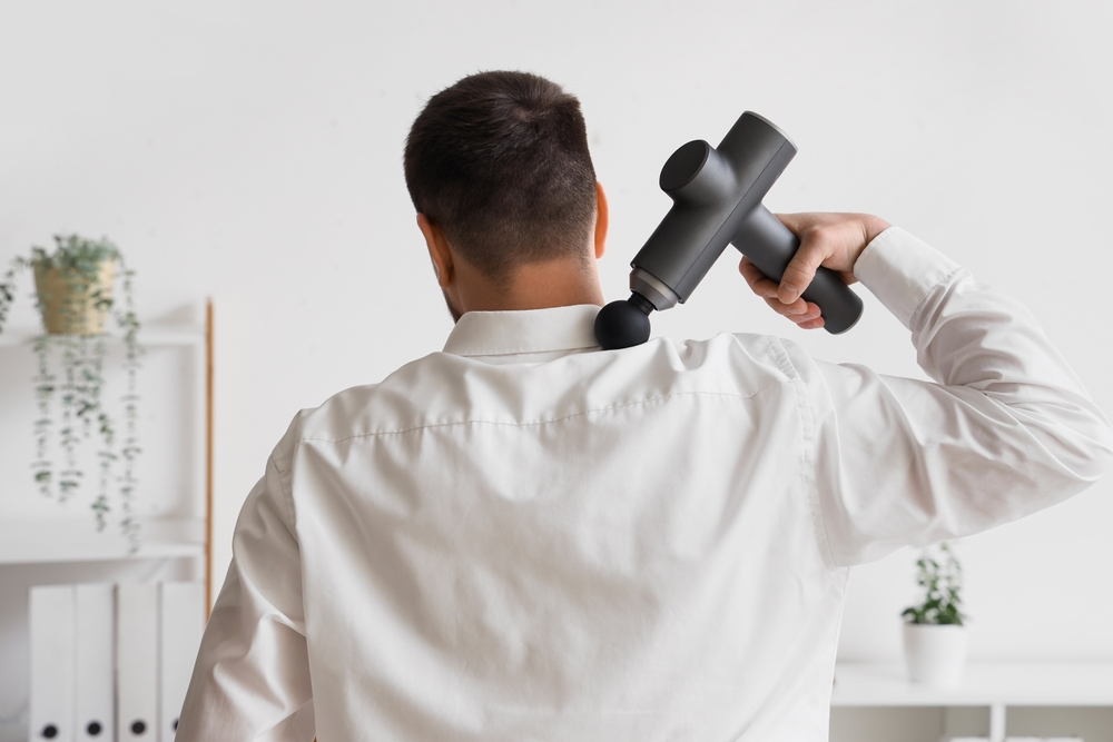 Office worker using a massage gun on neck muscles for pain relief